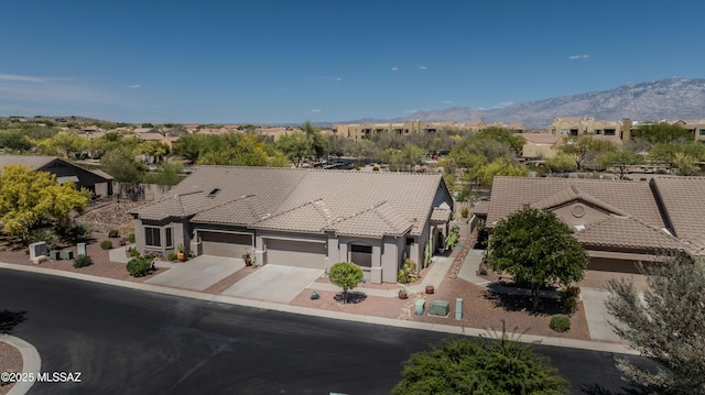 view of front of property featuring a tiled roof, an attached garage, a mountain view, driveway, and a residential view