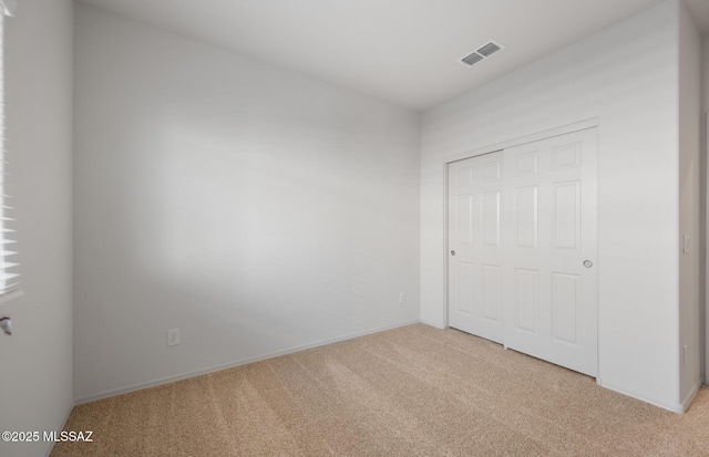 unfurnished bedroom with baseboards, visible vents, light carpet, and a closet