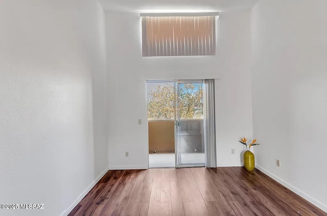 spare room featuring wood finished floors, baseboards, and a high ceiling