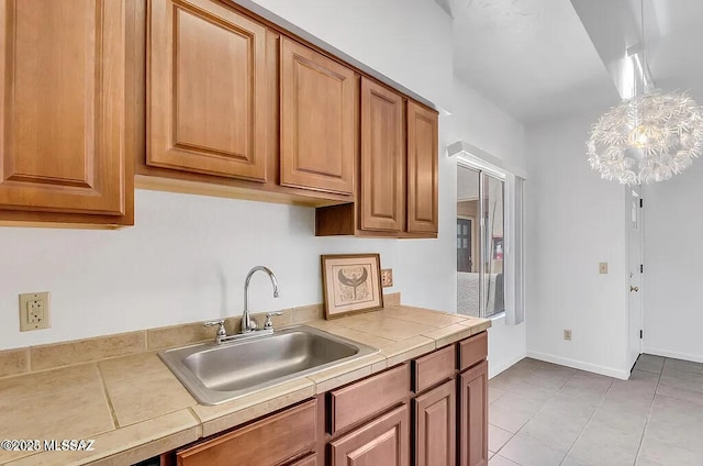 kitchen with tile counters, light tile patterned floors, brown cabinetry, and a sink