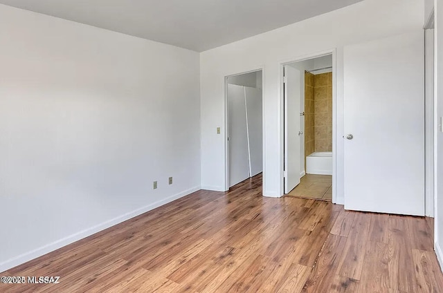 unfurnished bedroom featuring baseboards, ensuite bath, and light wood-style floors