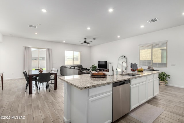 kitchen with stainless steel dishwasher, a sink, light wood-style flooring, a center island with sink, and white cabinetry
