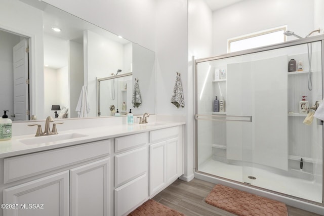 bathroom with a shower stall, double vanity, and wood finished floors