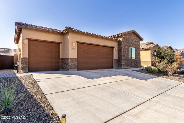 mediterranean / spanish-style house with an attached garage, stone siding, concrete driveway, stucco siding, and a tiled roof