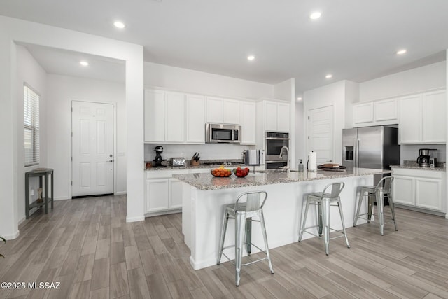 kitchen featuring stainless steel appliances, light wood-style floors, a kitchen bar, a center island with sink, and recessed lighting