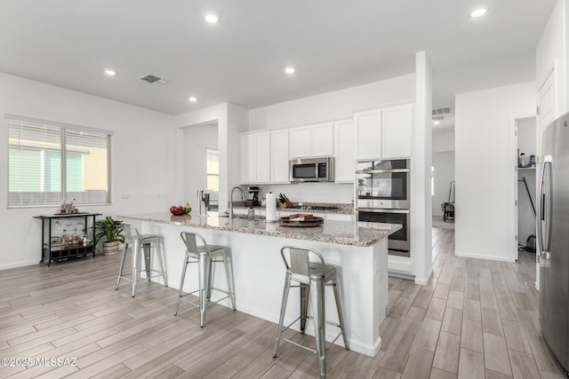 kitchen featuring appliances with stainless steel finishes, light wood-type flooring, a breakfast bar, white cabinets, and recessed lighting