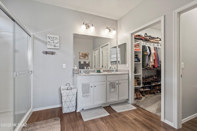 full bathroom with a sink, double vanity, a shower stall, and wood finished floors