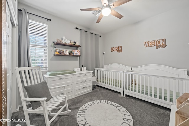bedroom featuring ceiling fan, a crib, and dark colored carpet