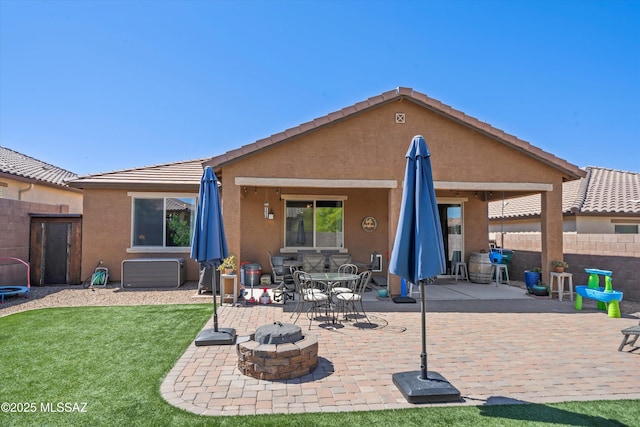 rear view of property featuring a fire pit, fence, a patio, stucco siding, and a lawn