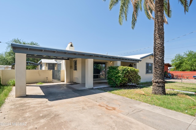 view of front of property featuring fence, stucco siding, a gate, a carport, and driveway