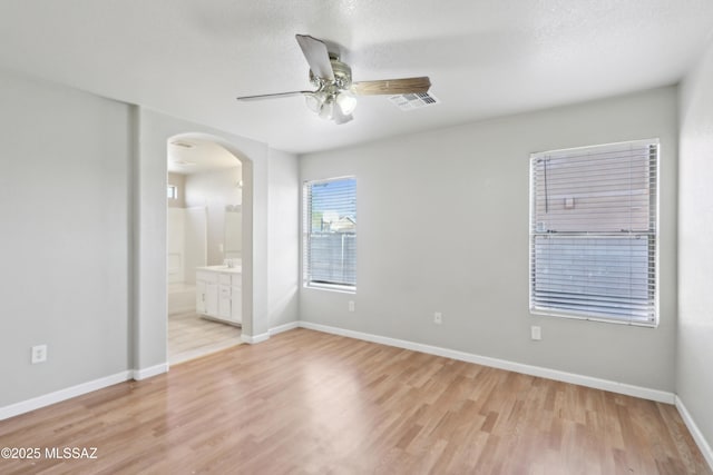 unfurnished bedroom featuring ensuite bath, arched walkways, baseboards, light wood-type flooring, and visible vents
