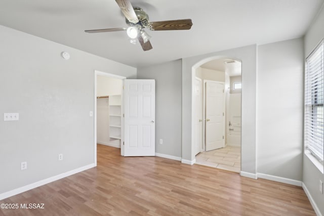 unfurnished bedroom with arched walkways, multiple windows, and light wood-type flooring