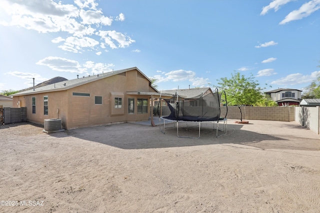 rear view of property with central air condition unit, a fenced backyard, a trampoline, and stucco siding