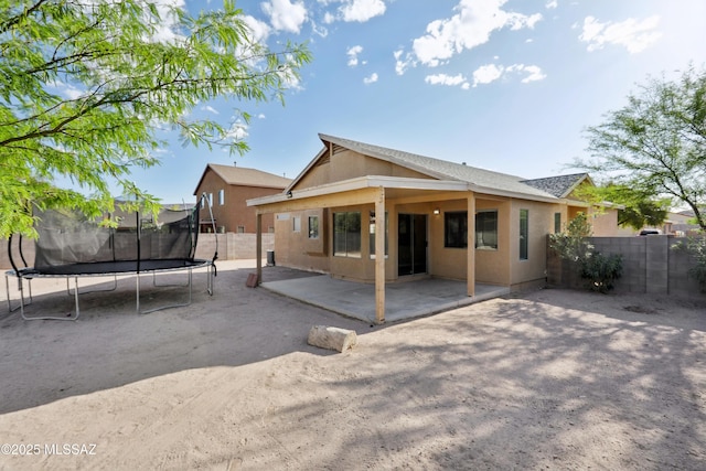 back of property featuring a patio, fence, a trampoline, and stucco siding