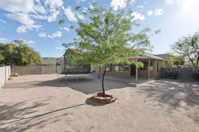 view of front of home featuring a fenced backyard, a trampoline, stucco siding, and a patio