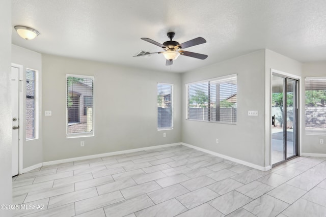 spare room featuring baseboards, a ceiling fan, a textured ceiling, and a wealth of natural light