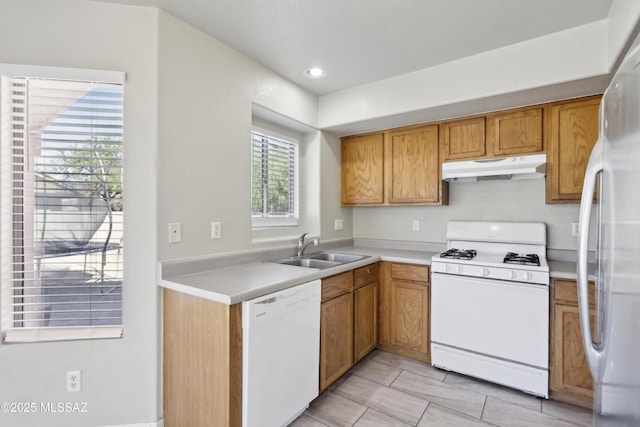 kitchen with white appliances, light countertops, under cabinet range hood, brown cabinets, and a sink