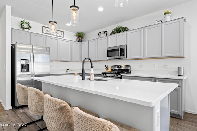 kitchen featuring appliances with stainless steel finishes, hanging light fixtures, light countertops, a kitchen breakfast bar, and wood finished floors