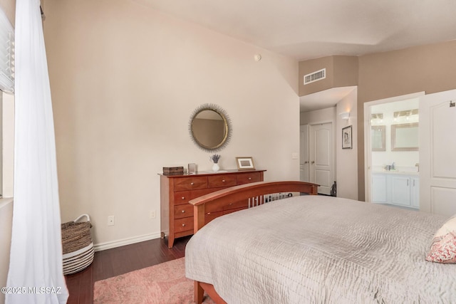bedroom with wood finished floors, lofted ceiling, baseboards, and connected bathroom