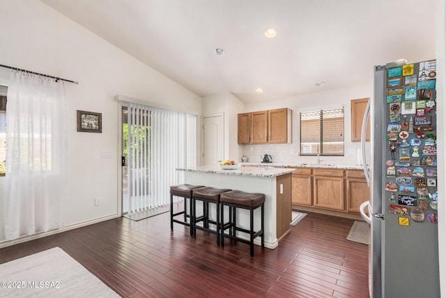 kitchen with freestanding refrigerator, a kitchen island, vaulted ceiling, a breakfast bar, and decorative backsplash