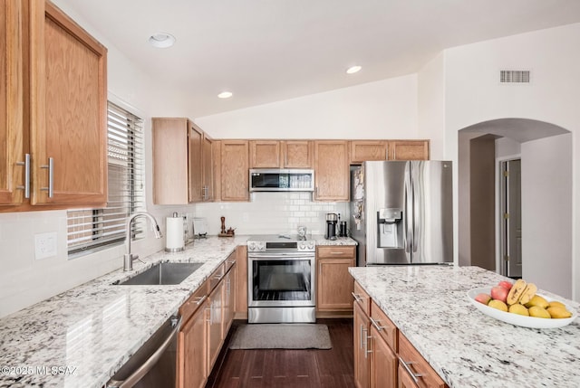 kitchen featuring appliances with stainless steel finishes, a sink, arched walkways, dark wood-type flooring, and light stone countertops