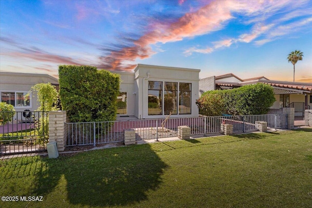 back of property at dusk with a lawn, stucco siding, and fence