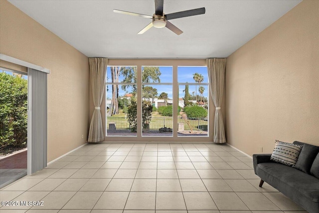 interior space with baseboards, a ceiling fan, a textured wall, and light tile patterned flooring