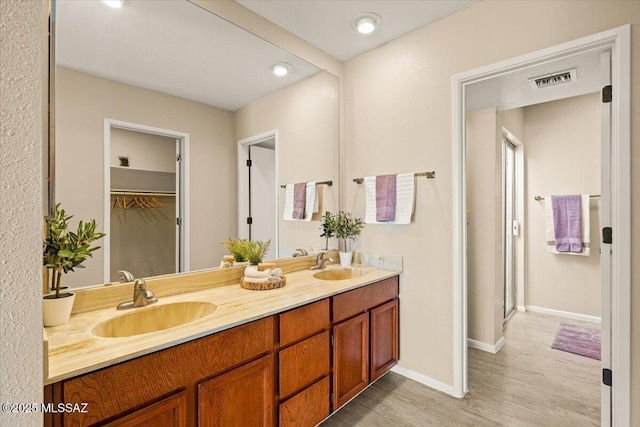 full bath with double vanity, a sink, baseboards, and wood finished floors