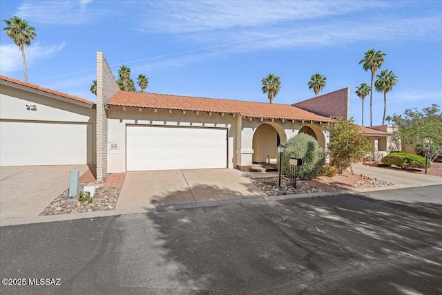 ranch-style home featuring an attached garage, stucco siding, driveway, and a tile roof