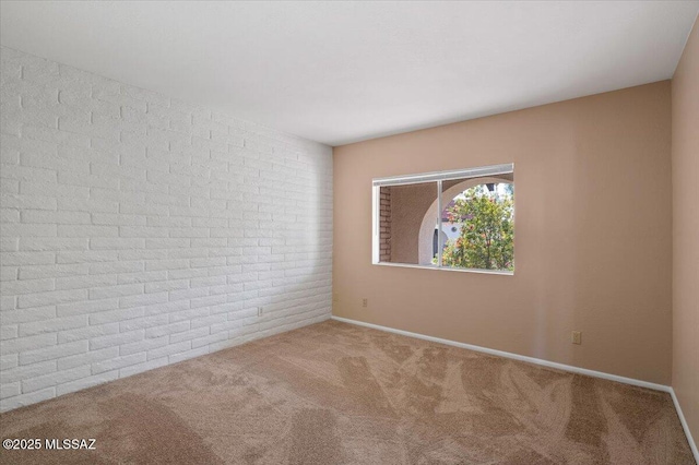 carpeted empty room featuring brick wall and baseboards