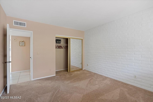 unfurnished bedroom with brick wall, visible vents, tile patterned flooring, carpet floors, and a closet