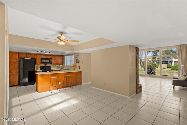 kitchen with a peninsula, open floor plan, light countertops, brown cabinets, and black appliances