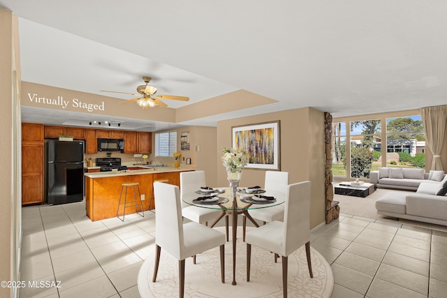 dining area featuring a ceiling fan, a tray ceiling, a wealth of natural light, and light tile patterned floors
