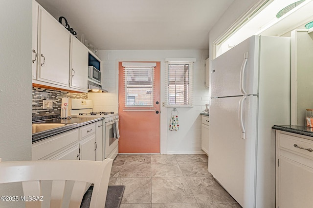 kitchen with dark countertops, tasteful backsplash, a sink, white appliances, and white cabinetry