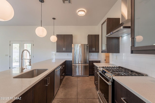 kitchen with wall chimney range hood, dark brown cabinetry, appliances with stainless steel finishes, a sink, and light countertops