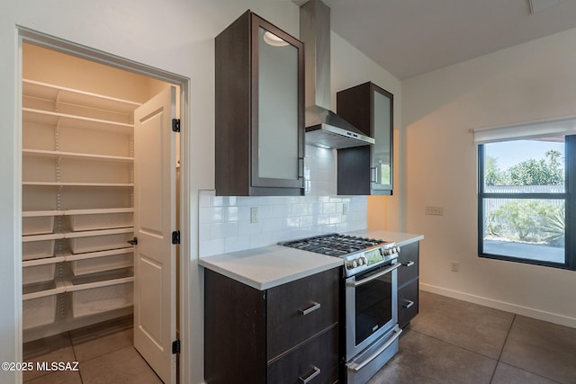 kitchen with stainless steel range with gas stovetop, light countertops, dark tile patterned floors, and wall chimney range hood