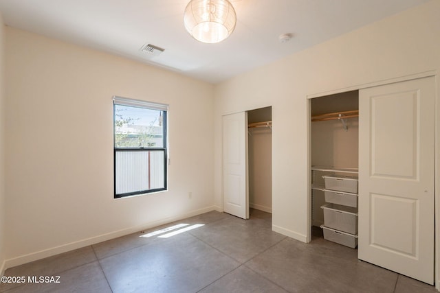 unfurnished bedroom featuring visible vents, baseboards, two closets, and finished concrete flooring