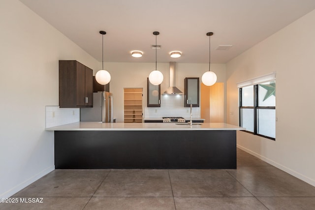kitchen featuring finished concrete flooring, light countertops, baseboards, freestanding refrigerator, and wall chimney exhaust hood