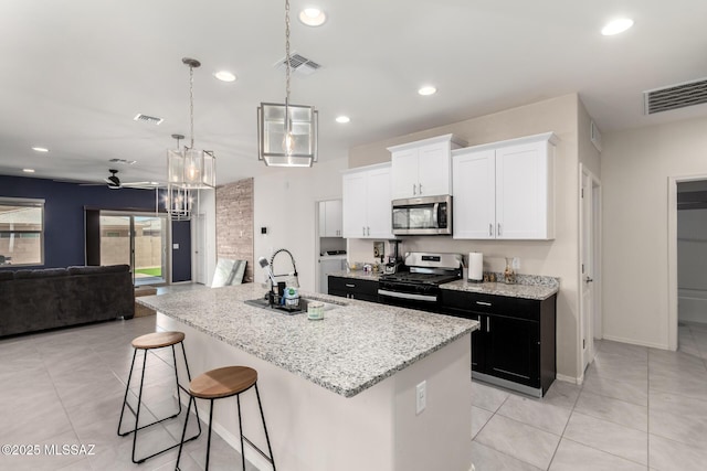7688 S Via Perfecta, Tucson, AZ 85756 - kitchen featuring appliances with stainless steel finishes, a sink, open floor plan, a kitchen island with sink, and light stone counters