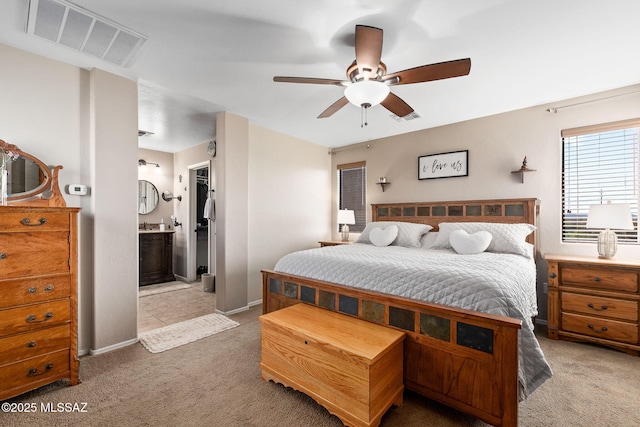carpeted bedroom featuring baseboards, a ceiling fan, ensuite bath, and visible vents