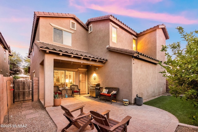 back of house at dusk featuring a patio, stucco siding, and a tile roof