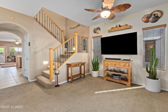 living area with carpet flooring, arched walkways, stairs, a ceiling fan, and baseboards