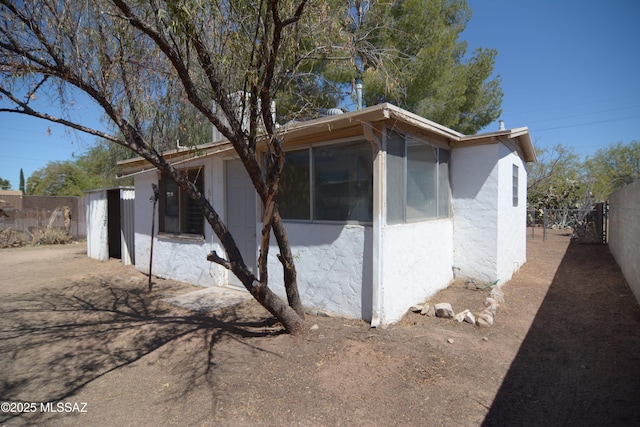 view of side of property with fence, stucco siding, and a sunroom
