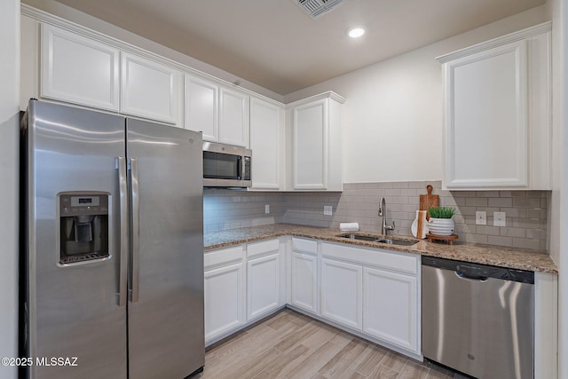 kitchen with light stone counters, a sink, stainless steel appliances, white cabinetry, and visible vents