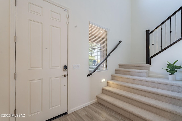 foyer entrance featuring baseboards, light wood finished floors, and stairway