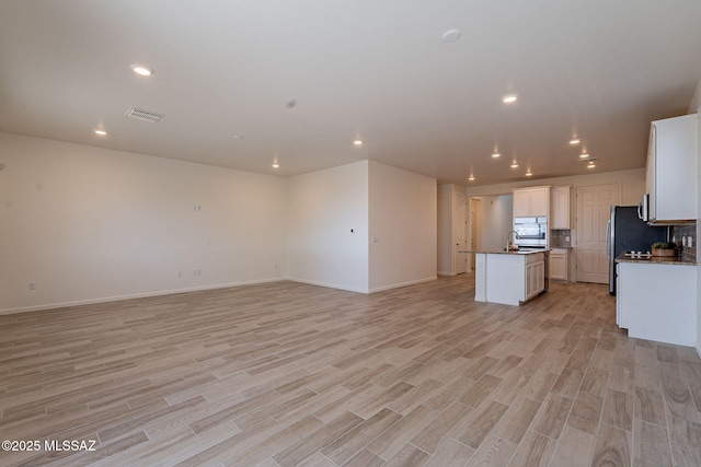 kitchen with a kitchen island with sink, visible vents, baseboards, light wood finished floors, and open floor plan