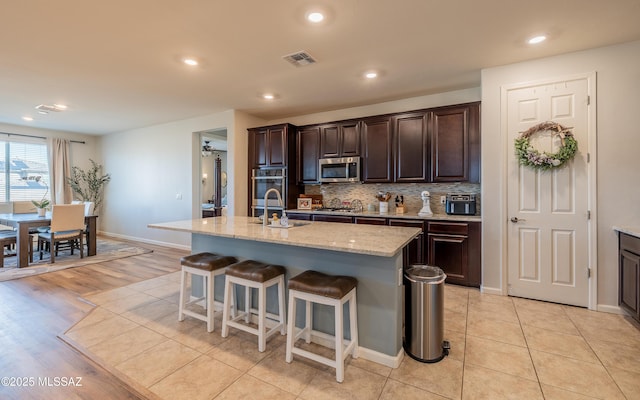 10199 S Pantano Knolls Dr, Vail, AZ 85641 - kitchen featuring visible vents, dark brown cabinets, a sink, stainless steel microwave, and a breakfast bar