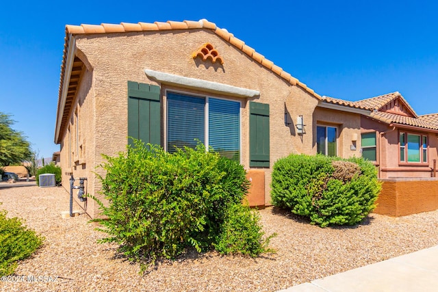 bungalow-style house with central air condition unit, stucco siding, and a tiled roof