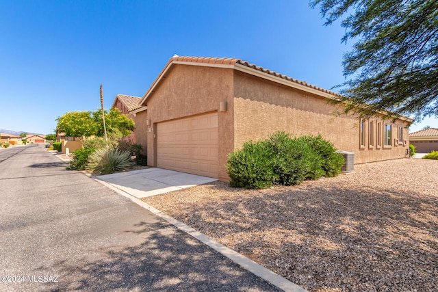 view of side of home featuring an attached garage, driveway, a tile roof, and stucco siding