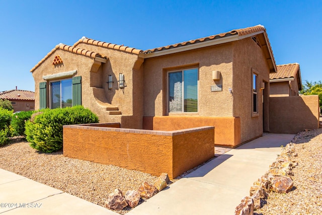 view of front of house with stucco siding, a tile roof, and fence